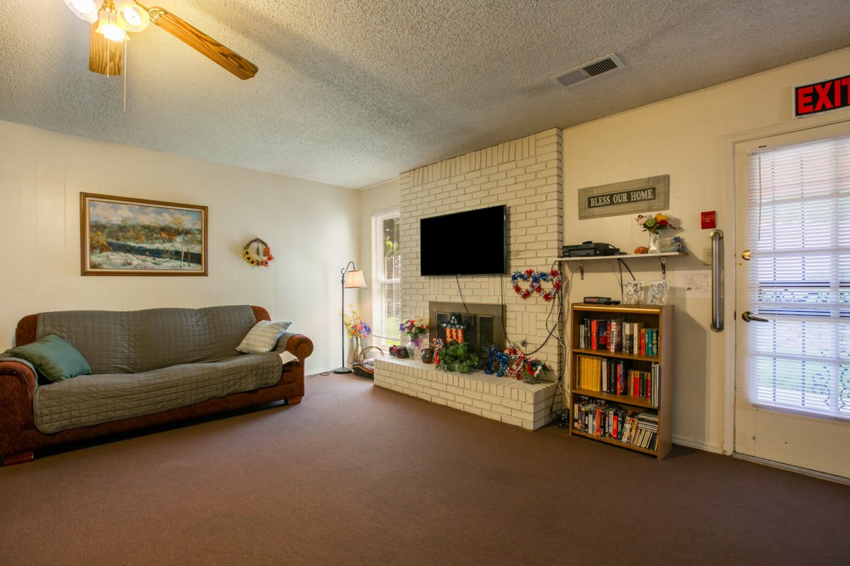 A cozy living room with a sofa, bookshelf, and a mounted television above the fireplace.