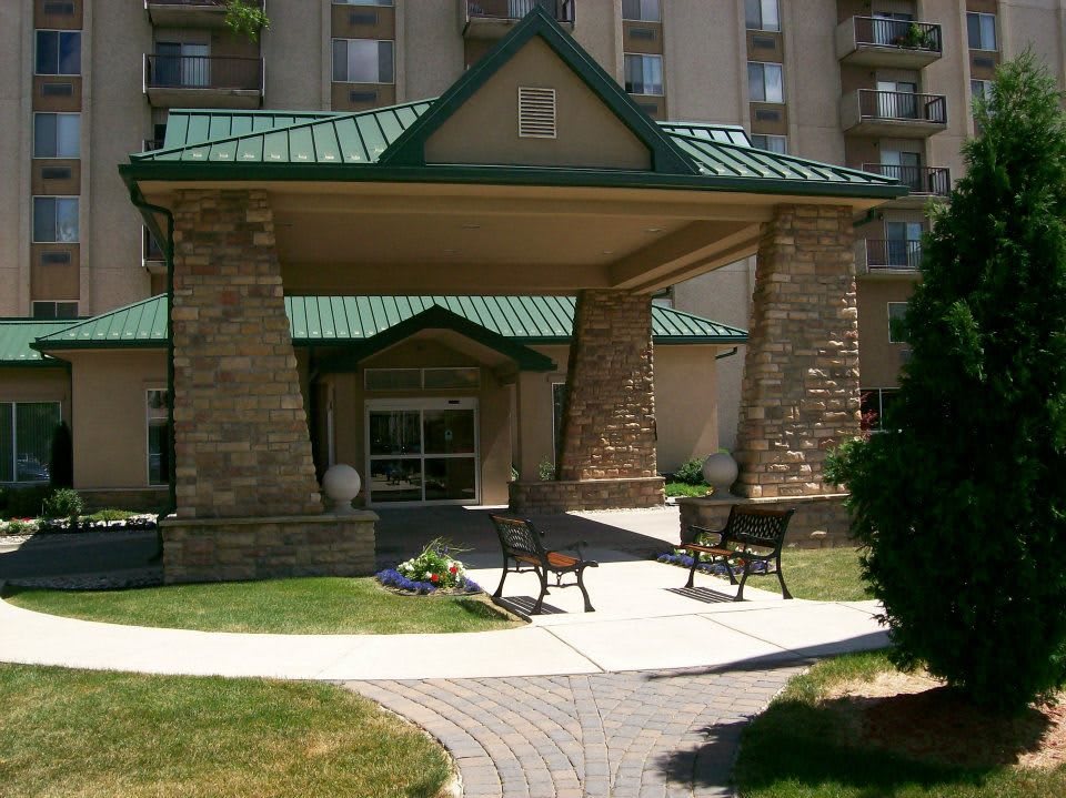 A picturesque hotel entrance with a green roof and stone pillars, featuring two benches on a landscaped pathway.