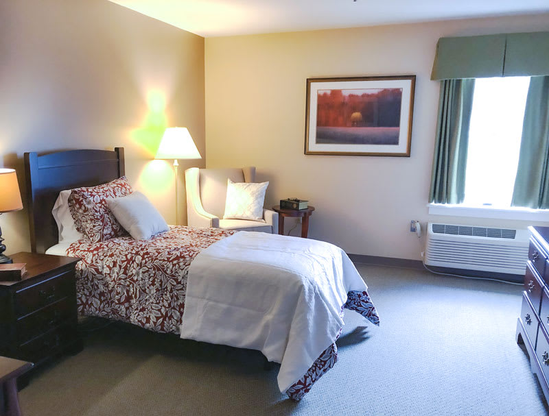 A cozy bedroom with a single bed, lamp, and framed artwork on the wall.