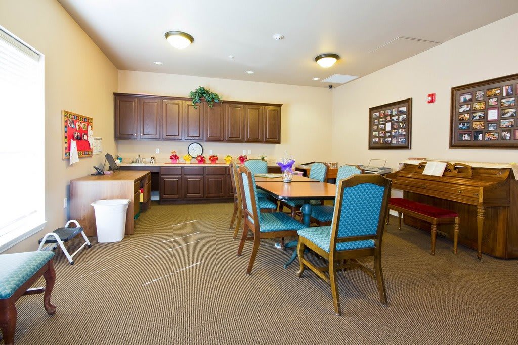 A well-lit dining area with a wooden table and upholstered chairs, featuring cabinetry and decorative items.