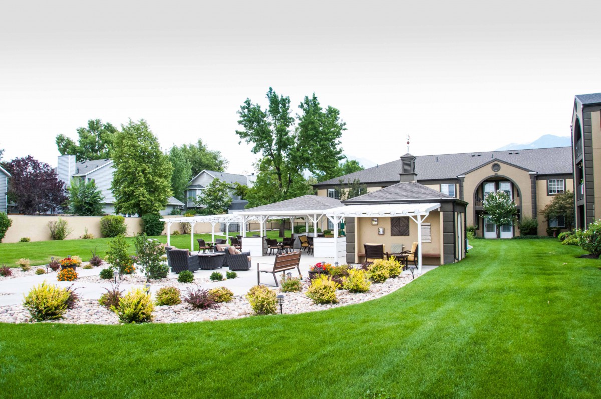 A beautifully landscaped garden featuring a pergola with outdoor seating, surrounded by lush greenery and well-maintained lawns.