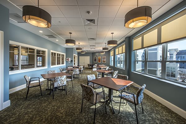 A modern dining room with neatly arranged tables and chairs, featuring large windows and contemporary lighting fixtures.