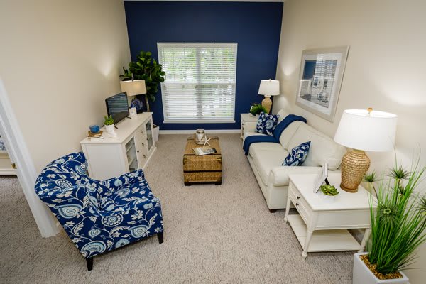 A cozy living room with a blue accent wall, featuring a white sofa, patterned armchair, and stylish decor.