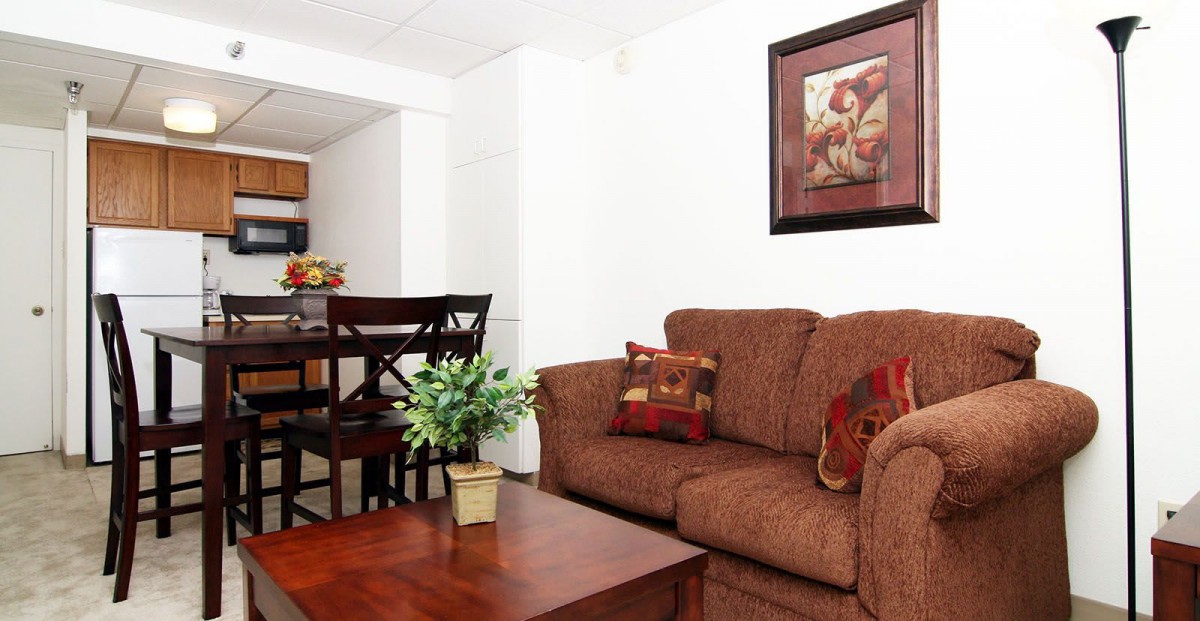 Cozy living room with a brown sofa, wooden coffee table, and dining area in the background.