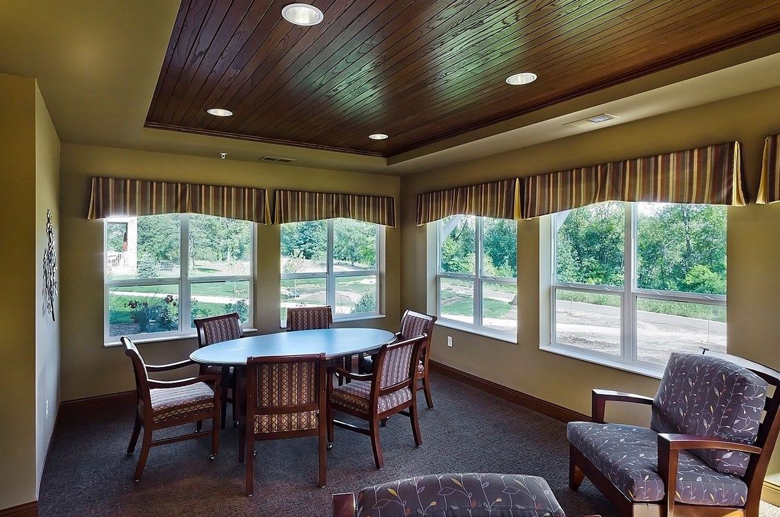 A cozy dining area with a round table surrounded by chairs and large windows letting in natural light.