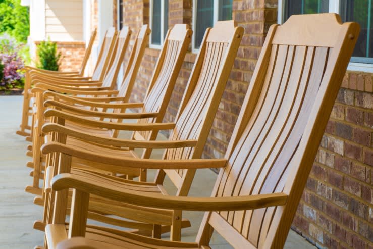 A row of wooden rocking chairs lined up on a porch beside a brick wall.