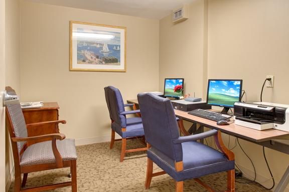 A small office with two computers on desks and blue chairs, featuring a wall painting.
