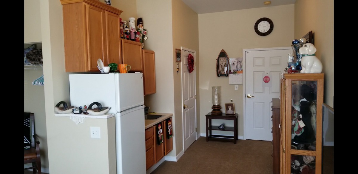 A cozy apartment kitchen with wooden cabinets and a white refrigerator, featuring decorative items and a small side table near the door.