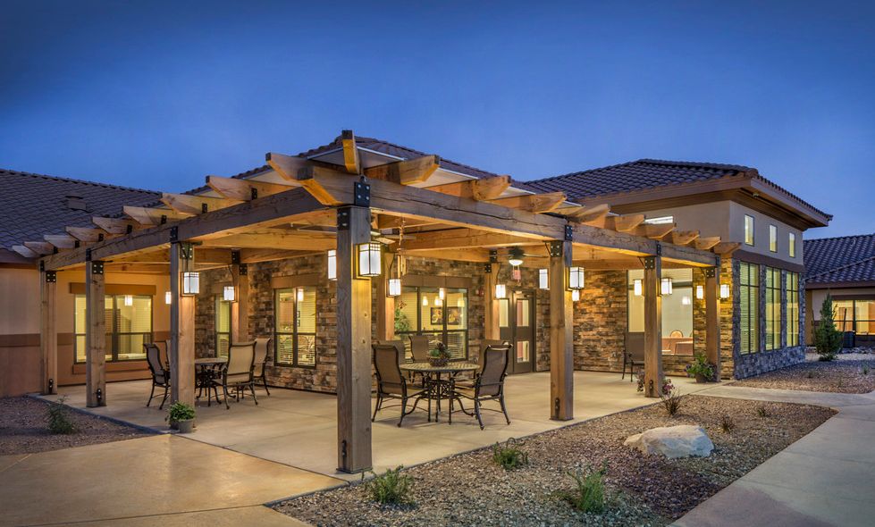 A cozy outdoor patio area with a pergola, complete with tables and chairs, illuminated by warm lights during the evening.