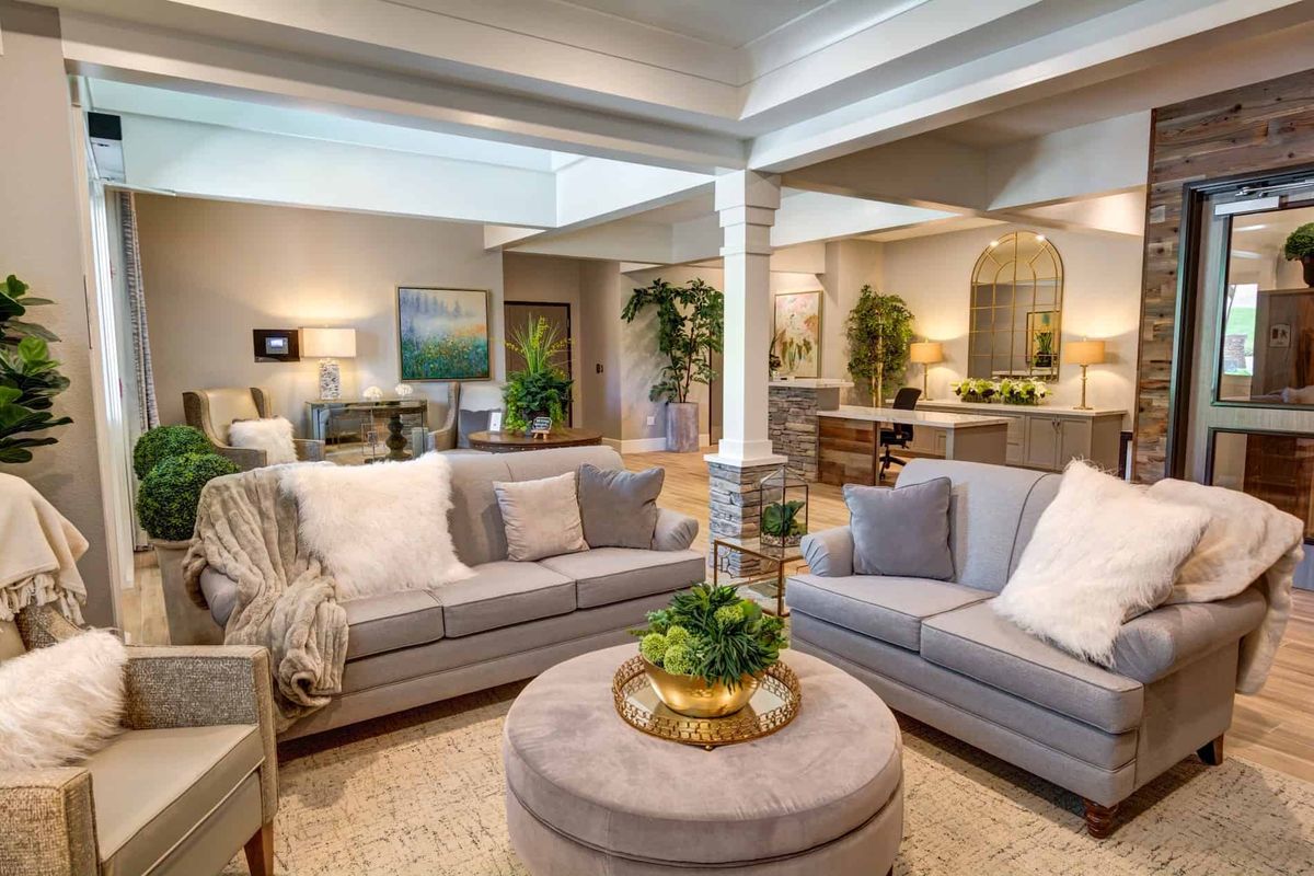 A spacious and well-decorated living room with gray sofas, a central coffee table, and indoor plants.