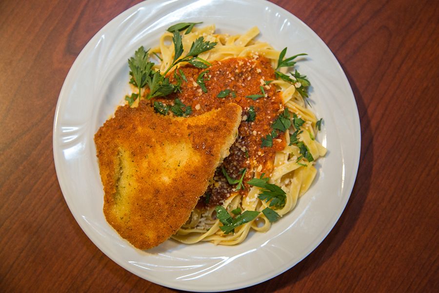 A plate of chicken parmesan served over pasta with marinara sauce and garnished with fresh parsley.