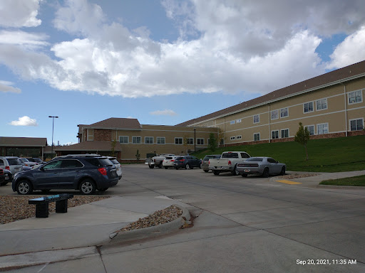 A view of a large building with a parking lot filled with vehicles under a partly cloudy sky.