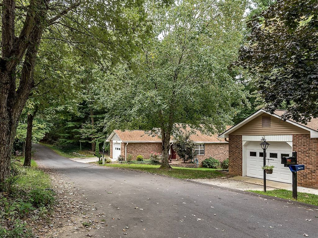 A suburban house surrounded by trees along a quiet road.