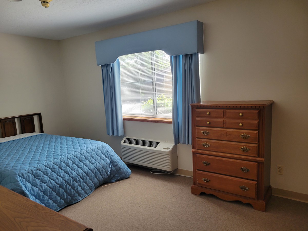 A bedroom with blue bedding and curtains, featuring a wooden dresser and a window.