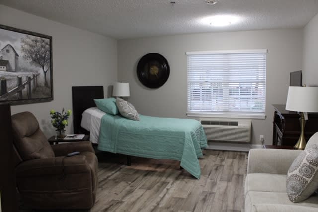 A minimalist bedroom with a single bed, bedside table, and window blinds.