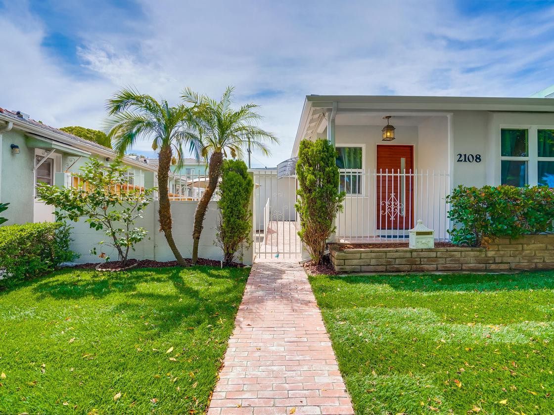 A charming house with a red door, surrounded by a lush front yard and palm trees.