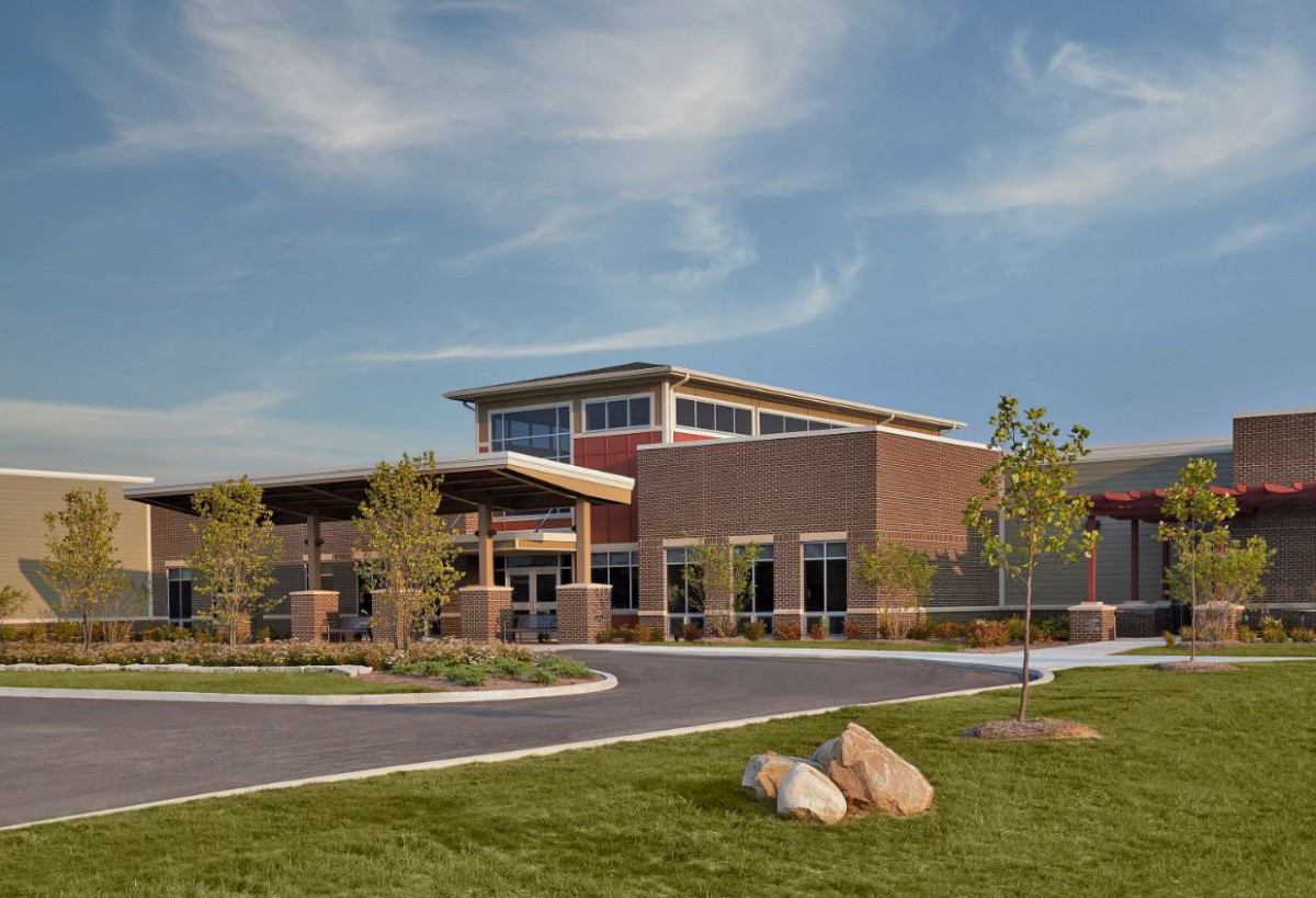 A modern school building with a brick exterior surrounded by landscaped grounds under a clear blue sky.