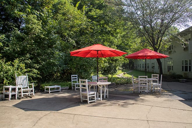 A sunny outdoor patio area with red umbrellas, surrounded by greenery.