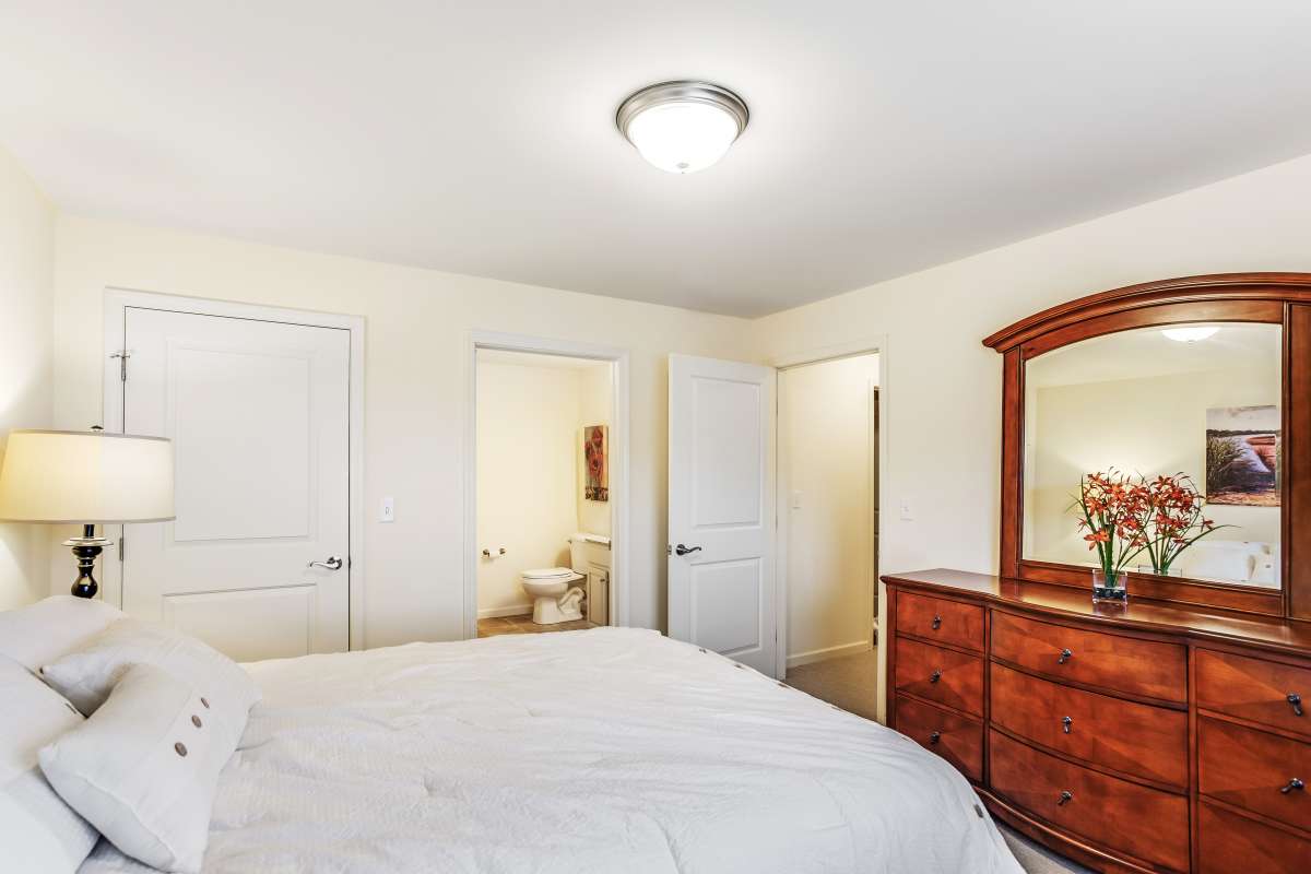 A cozy bedroom featuring a bed, dresser with mirror, and warm lighting.
