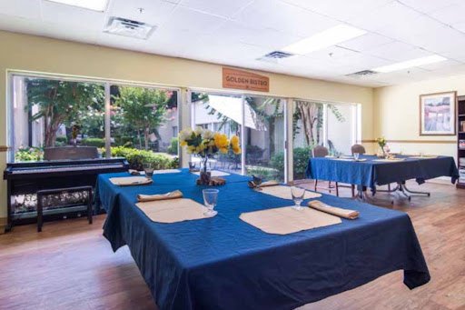 A cozy dining area featuring blue table settings and vibrant floral arrangements, illuminated by natural light.