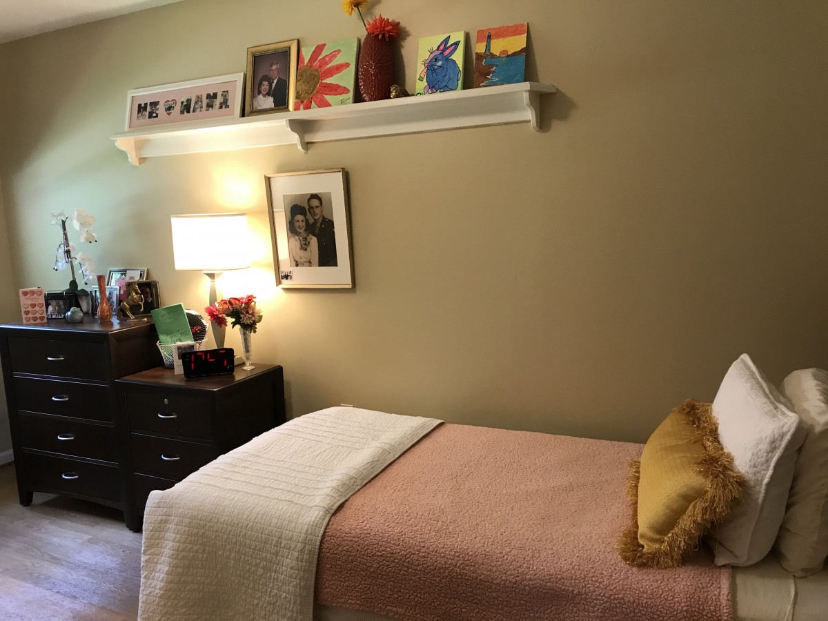 A cozy bedroom with a single bed, decorated with artwork and a lamp on the dresser.