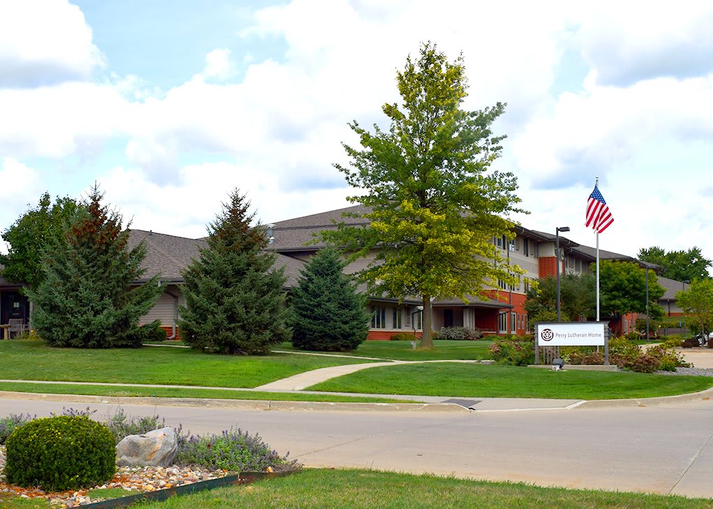 A two-story office building surrounded by trees and a well-kept lawn, featuring an American flag and a sign at the entrance.