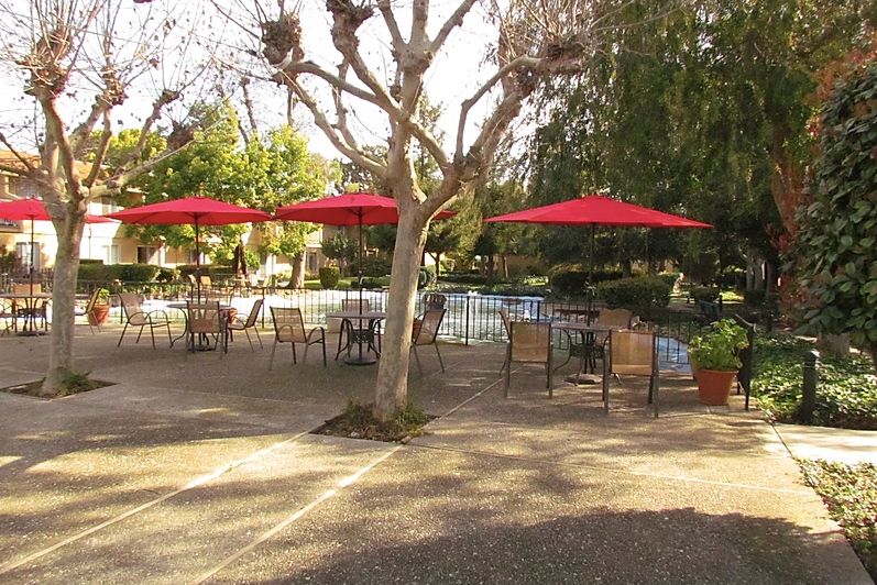 Outdoor seating area with red umbrellas and a pool.