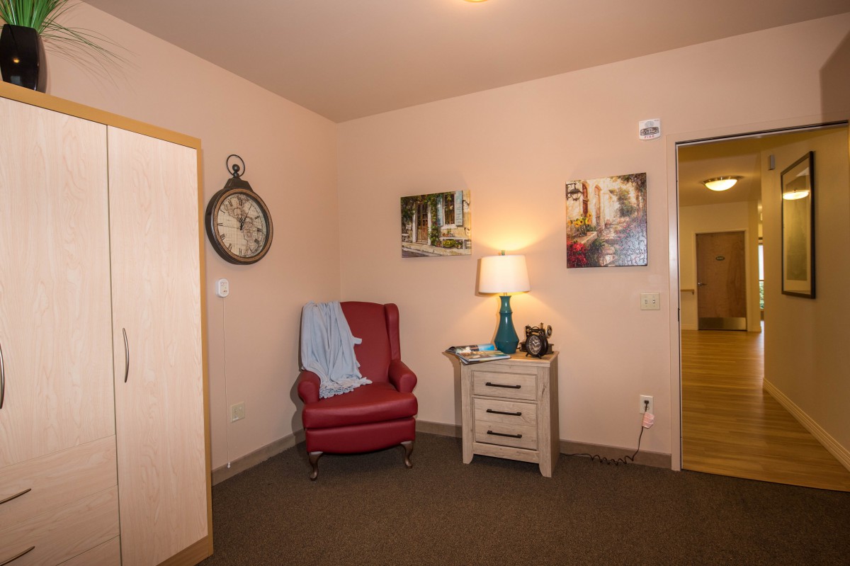 A cozy living room corner with a red armchair, side table, and decorative elements including a clock and wall art.