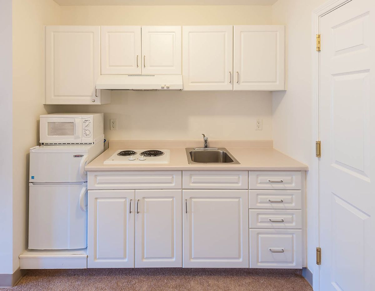 A compact kitchen area with white cabinets, a microwave, stovetop, and sink.