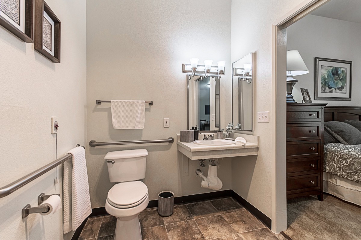 A modern bathroom with a toilet, sink, and mirror, featuring contemporary lighting and tile flooring.