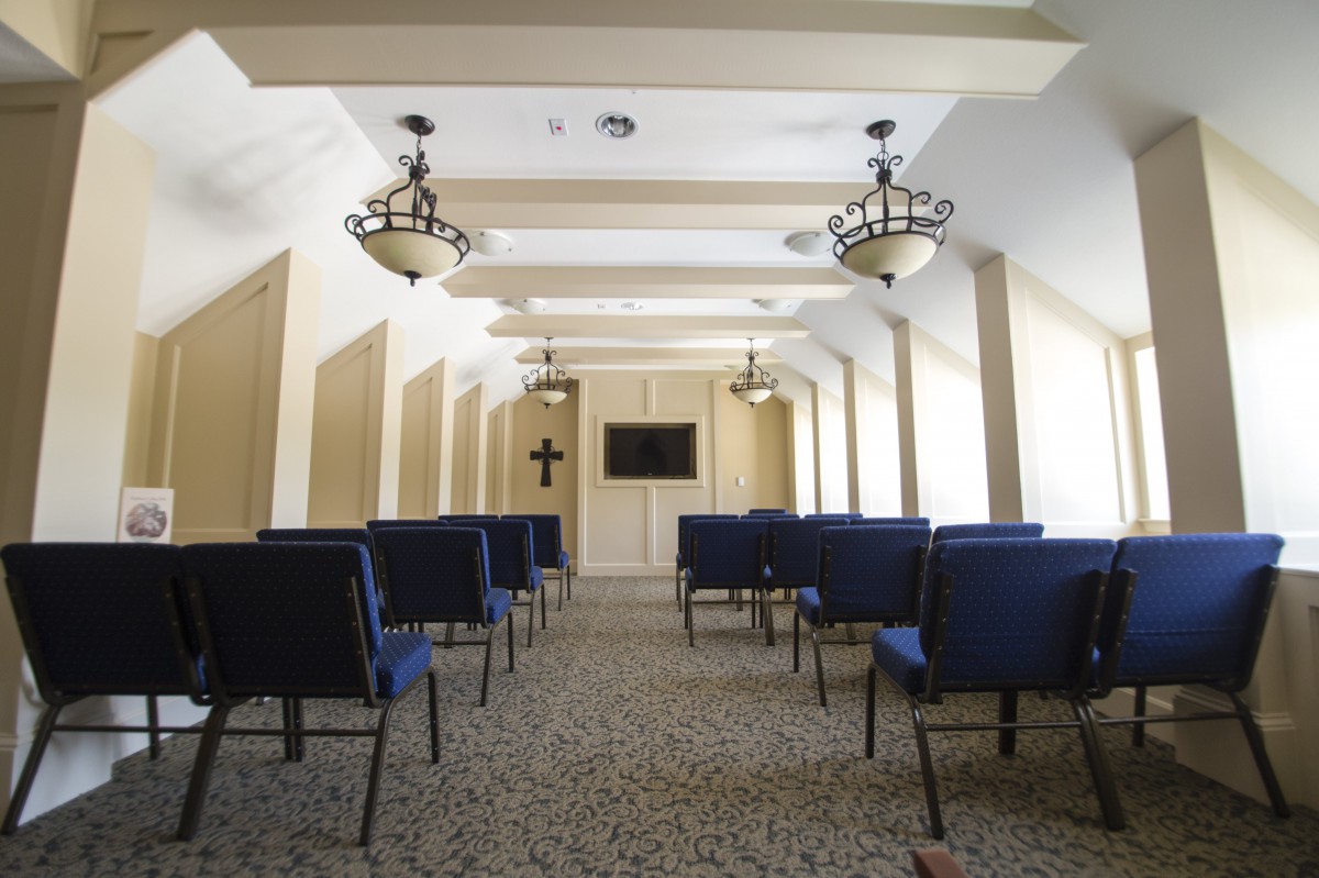 A small chapel with rows of chairs, a cross on the wall, and elegant lighting fixtures.