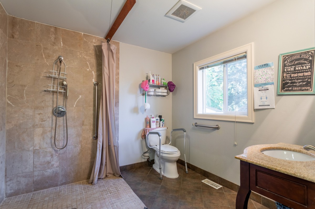 A modern bathroom featuring a shower, toilet, and sink with natural light from a window.