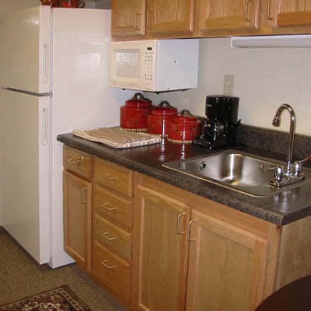 A compact kitchen with wooden cabinets, a refrigerator, microwave, and various appliances on the countertop.