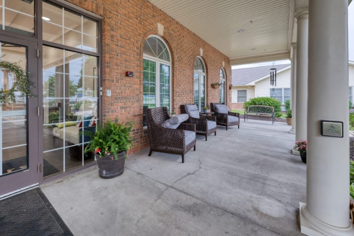 A cozy patio area with wicker chairs and potted plants against a brick wall.