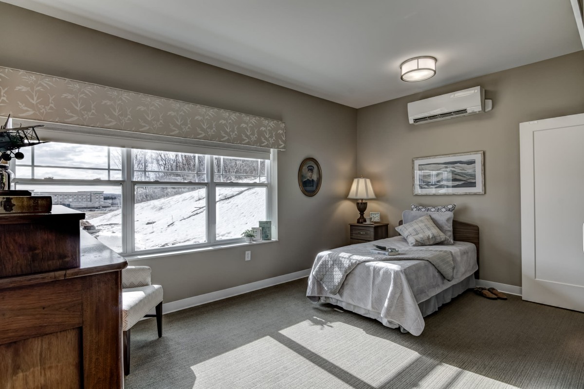 A minimalist bedroom with a single bed, large window, and neutral colors.