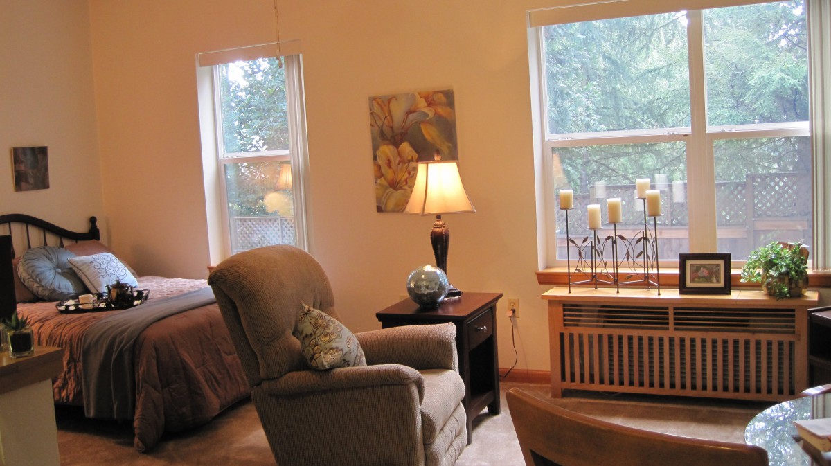 A cozy living room with an armchair, lamp, and large windows allowing natural light.