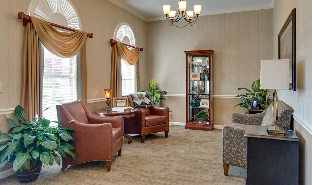 A cozy living room with armchairs, a bookshelf, and decorative plants.