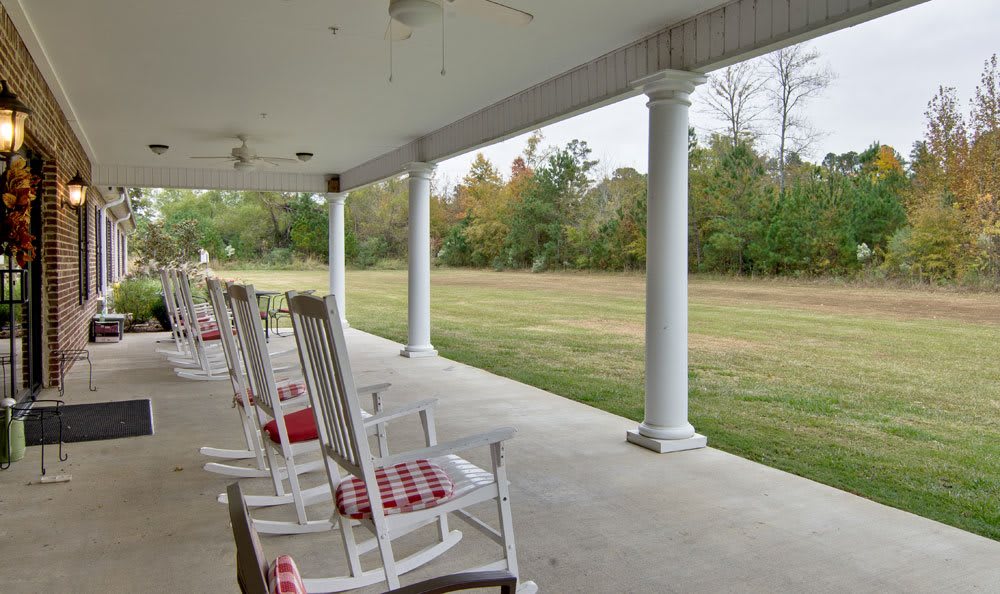 A peaceful porch with rocking chairs overlooking a grassy area.