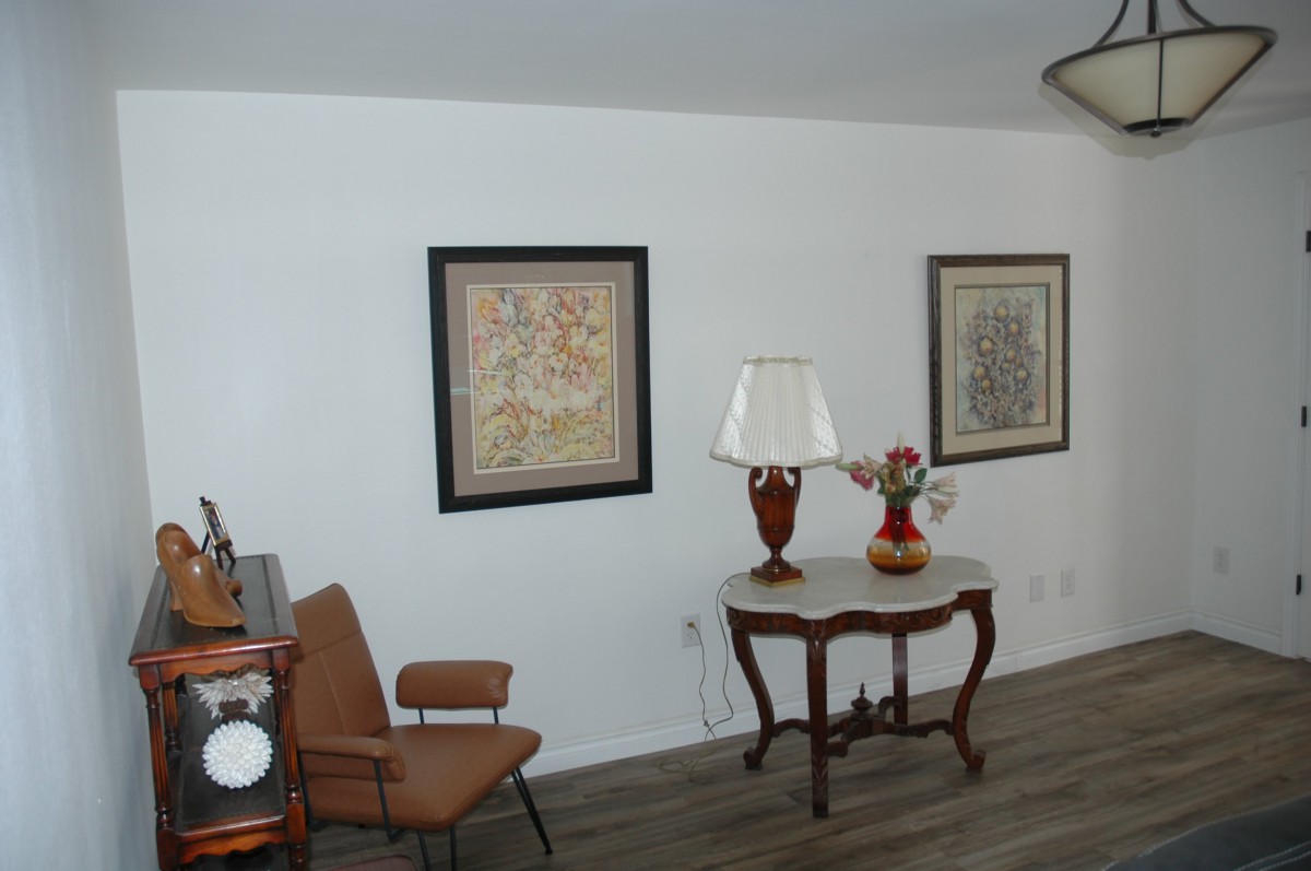 A living room interior featuring a table with a lamp and decorative vase, chairs, and framed artwork on the walls.