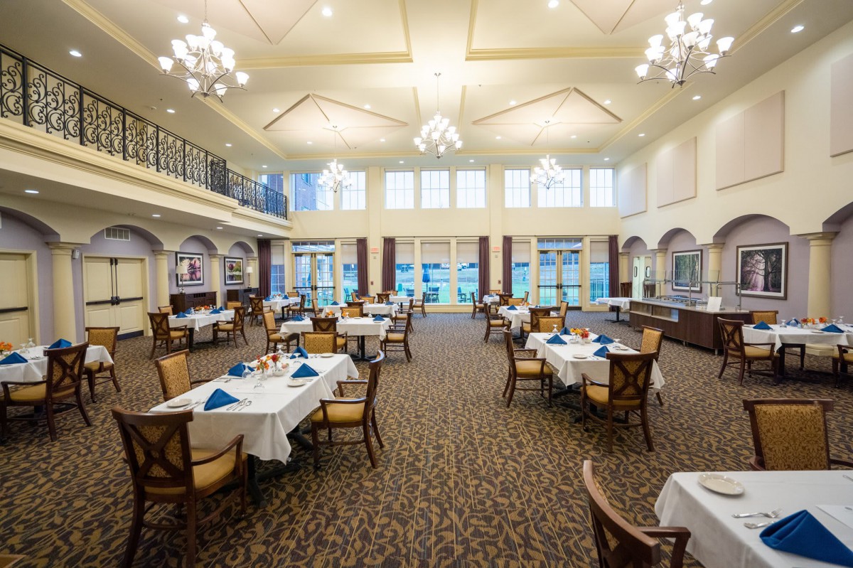 An elegant dining room with chandeliers and large windows, featuring neatly arranged tables and chairs.