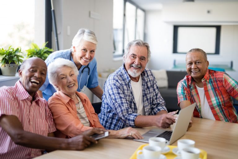 A group of seniors smiling and gathered around a laptop in a casual meeting setting.