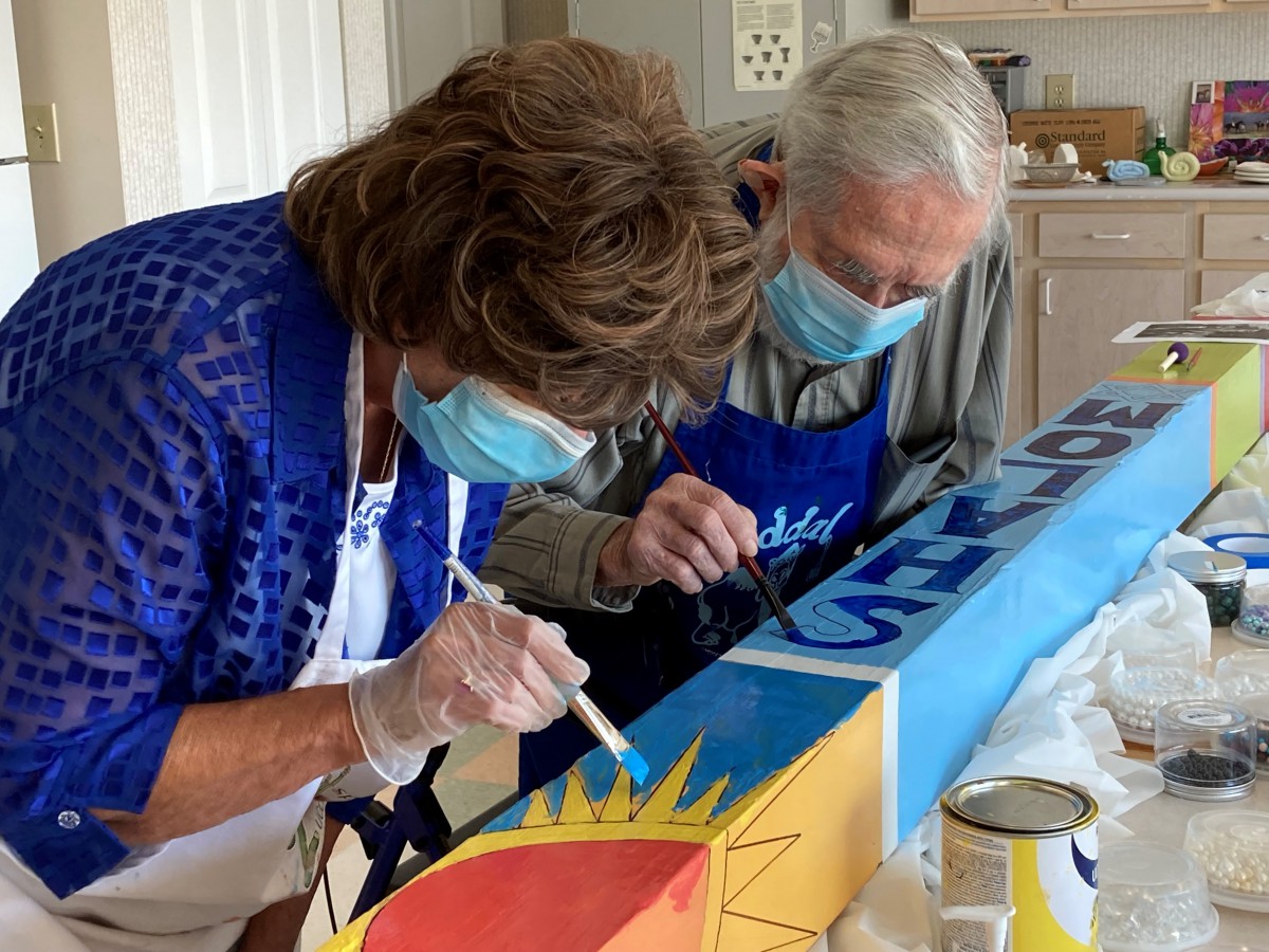 Two people wearing masks engage in a collaborative painting project.