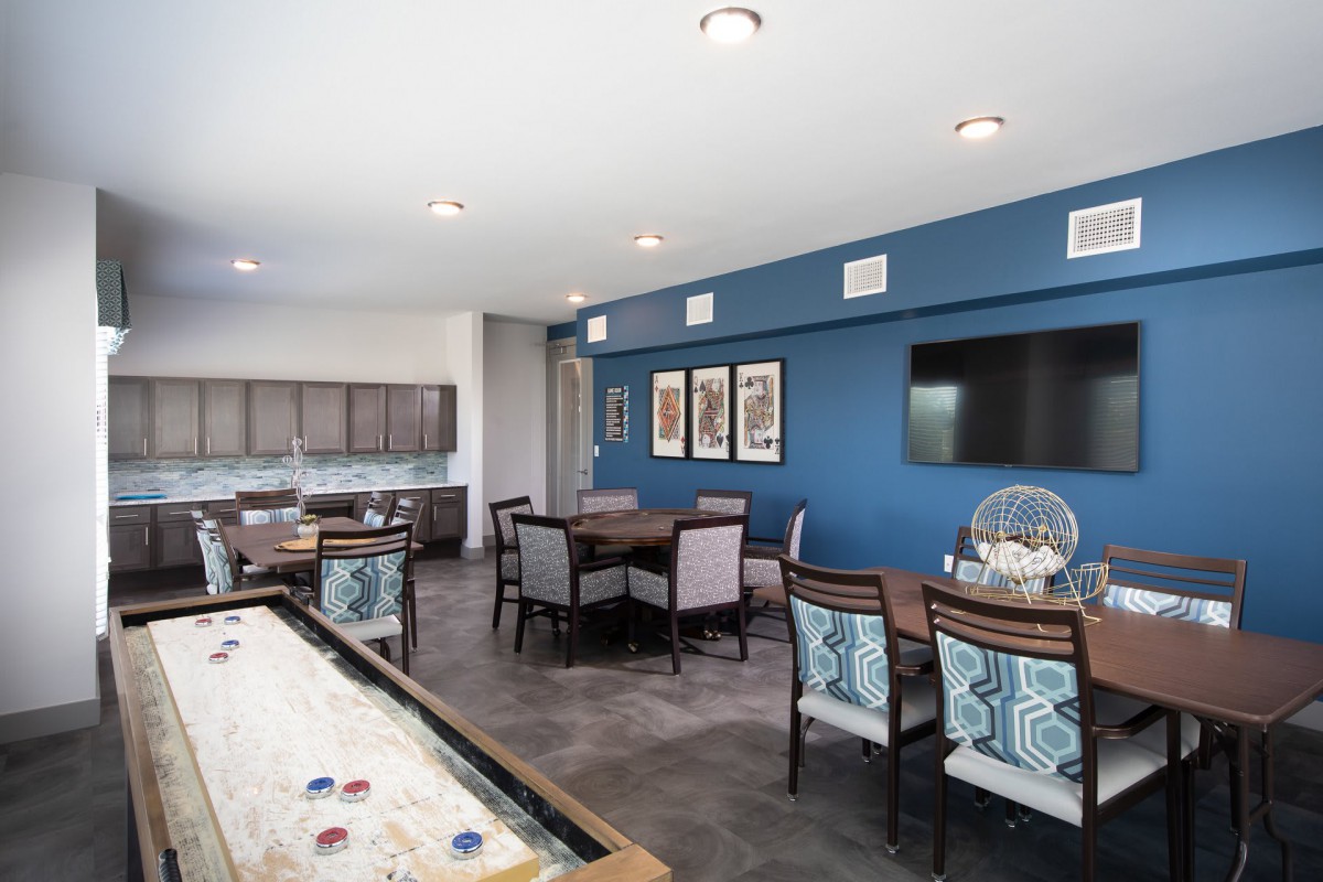 A modern and stylish game room featuring a shuffleboard table, comfortable seating, and a large screen TV against a blue accent wall.