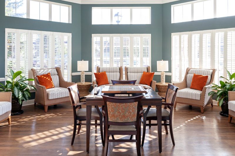 A modern dining room with large windows, featuring wooden furniture and orange accent pillows.