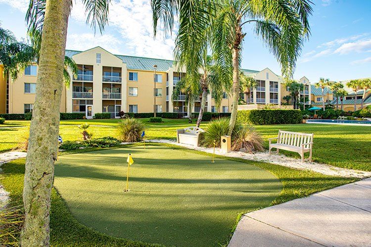 A sunny resort with a putting green, surrounded by palm trees and apartment-style buildings.