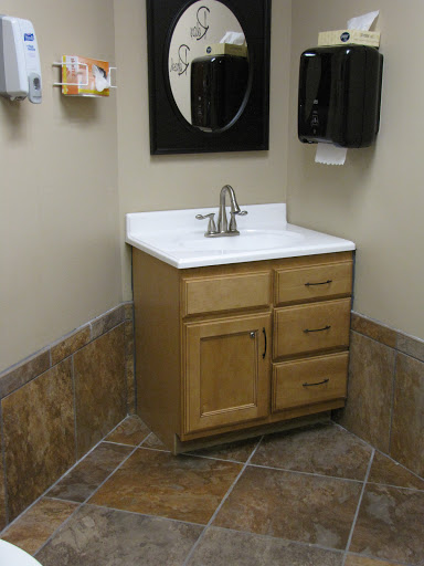 A corner bathroom sink with wooden cabinetry and a mirror above it.