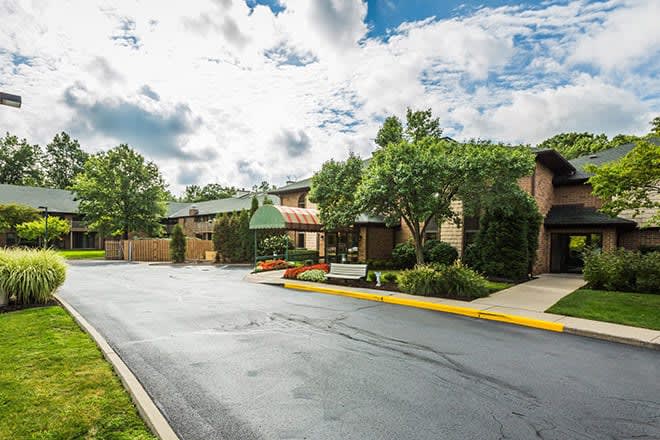 A well-maintained suburban building with trees and a paved road under a partly cloudy sky.