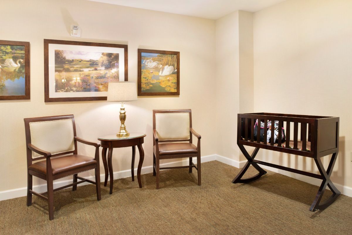 A cozy waiting area with chairs, a small table with a lamp, wall art, and a crib.