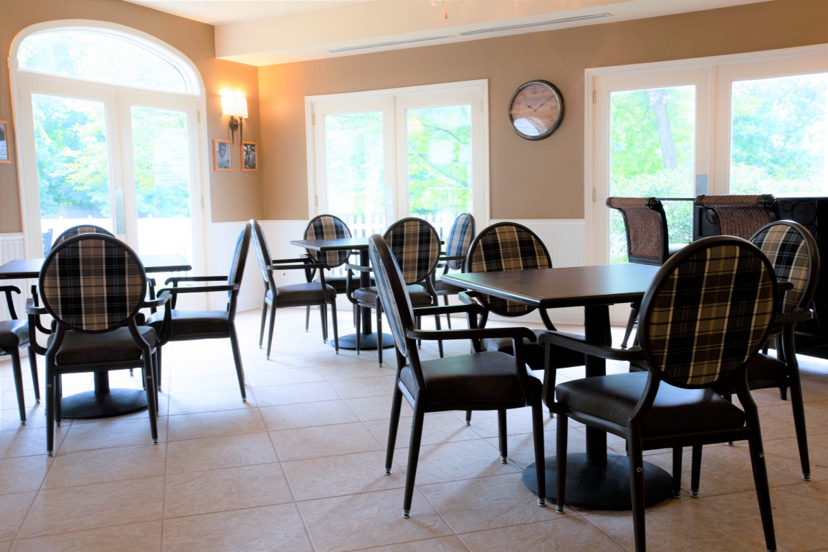 A well-lit dining area with tables and chairs arranged neatly by large windows.