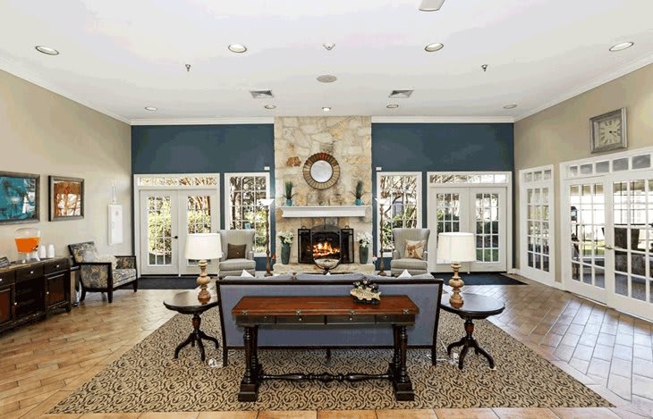 A spacious living room featuring a central fireplace, surrounded by elegant furniture and ample natural light from large windows.